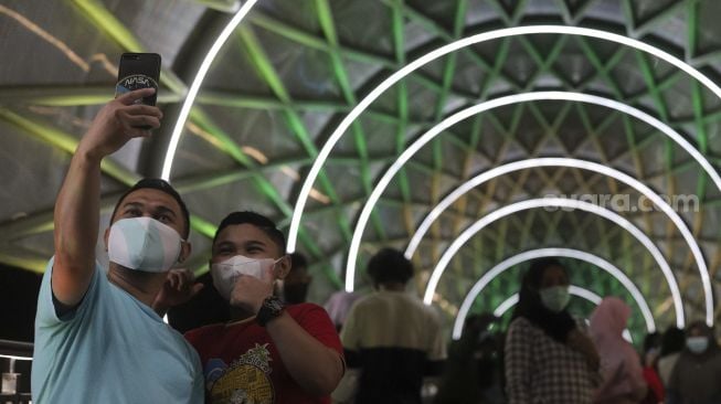 Warga berswafoto di Jembatan Penyeberangan Orang (JPO) Lenteng Agung, Jakarta, Minggu (5/9/2021) malam. [Suara.com/Angga Budhiyanto]