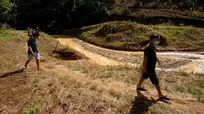 Sejumlah warga melintas di dekat anak sungai yang diduga tercemar lumpur mengandung bahan kimia berbahaya di lahan pertanian warga di Desa Kanaan, Bolaang Mongondow, Sulawesi Utara, Jumat (10/92021). ANTARA FOTO/Adwit B Pramono
