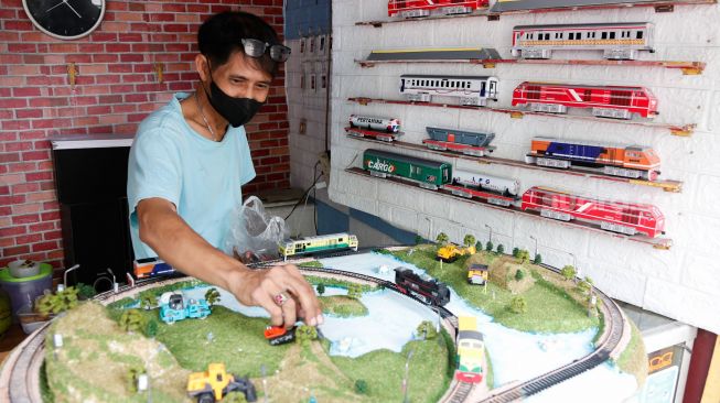 Iskandar (53) membuat diorama dengan hasil miniatur kereta api yang dibuatnya di kiosnya kawasan Manggarai, Jakarta Selatan, Sabtu (11/9/2021). [Suara.com/Alfian Winanto]