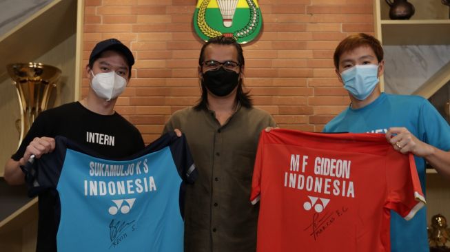 Kevin Sanjaya Sukamuljo / Marcus Fernaldi Gideon memberi hadiah jersey kepada seniman asal Batam, Sofian (tengah) yang membuat karya seni bergambarkan lukisan wajah The Minions dengan bahan shuttlecock bekas. [Dok. PBSI]