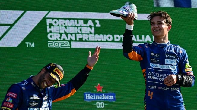 Pebalap McLaren yang finis kedua di F1 GP Italia 2021, Lando Norris (kanan) dan rekan setimnya yang meraih podium kemenangan, Daniel Ricciardo menaiki podium di Sirkuit Autodromo Nazionale di Monza, 12 September 2021. ANDREJ ISAKOVIC / AFP.