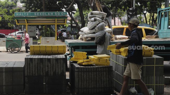 Pekerja menurunkan material proyek revitalisasi trotoar di Jalan Senopati, Kebayoran Baru, Jakarta, Rabu (15/9/2021). [Suara.com/Angga Budhiyanto]