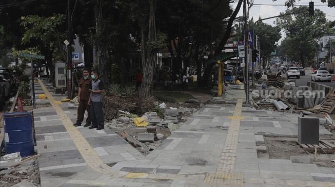 Warga berdiri di dekat proyek revitalisasi trotoar di Jalan Senopati, Kebayoran Baru, Jakarta, Rabu (15/9/2021). [Suara.com/Angga Budhiyanto]