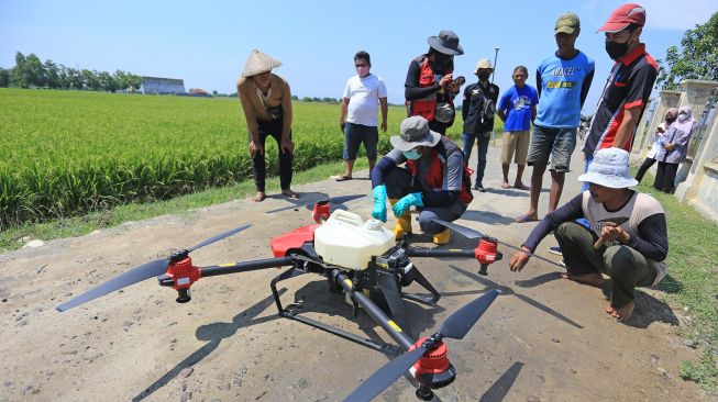 Petani melihat teknisi saat mengoperasikan pesawat tanpa awak (Drone) yang digunakan untuk menyemprotkan cairan pestisida di areal sawah desa Krangkeng, Kecamatan Krangkeng, Indramayu, Jawa Barat, Kamis (16/9/2021).  ANTARA FOTO/Dedhez Anggara