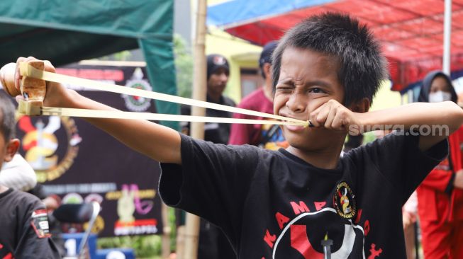 Ekspresi seorang anak saat membidik target ketika mengikuti kompetisi ketapel di Kampung Ketapel, Ciganjur, Jakarta Selatan, Minggu (19/9/2021). [Suara.com/Alfian Winanto]