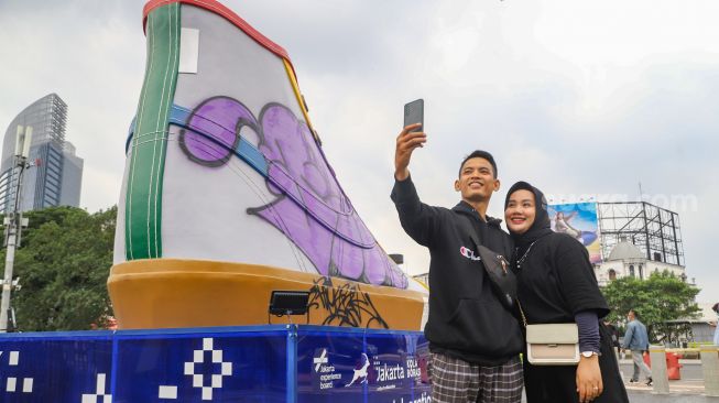 Warga berswafoto dengan latar belakang Tugu Sepatu di Stasiun BNI City, Jakarta Pusat, Minggu (19/9/2021). [Suara.com/Alfian Winanto]