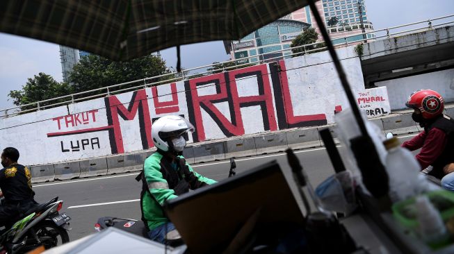 Pengendara motor melintas di depan mural yang berisi kritikan di Jakarta Barat, Minggu (19/9/2021).  ANTARA FOTO/Sigid Kurniawan