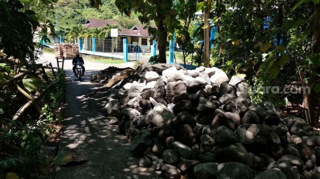 Sejumlah bongkahan batu menutup akses jalan menuju pabrik PT Yogyakarta Isti Parama (YIP) usai tidak adanya kejelasan perusahaan membayar uang sewa ke Pemdes Srimulyo, Rabu (21/4/2021). [tim Suara.com]