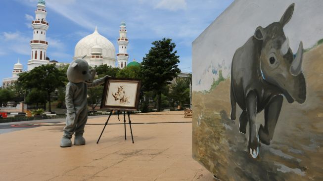 Pemuda dengan kostum badak sumatera menunjukkan lukisan badak sumatera saat kegiatan kampanye kreatif memperingati hari badak sedunia di Taman Ratu Safiatuddin, Banda Aceh, Aceh, Rabu (22/9/2021). ANTARA FOTO/Syifa Yulinnas