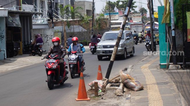 Pengendaraan sepeda motor melintas di samping tiang miring di Jl Wr Supratman Ciputat Timur, Tangerang Selatan. Rabu (22/9).  [Suara.com/ Hilal Rauda Fiqry]