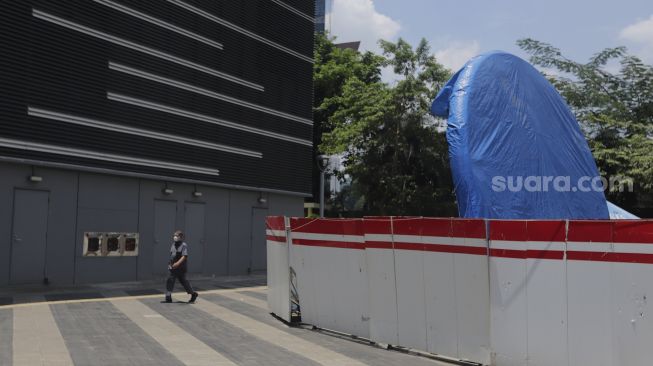 Warga berjalan di dekat proyek pembangunan tugu sepeda di jalur pedestrian Jalan Jenderal Sudirman, Jakarta, Rabu (22/9/2021). [Suara.com/Angga Budhiyanto]