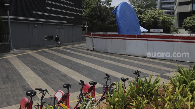 Warga berjalan di dekat proyek pembangunan tugu sepeda di jalur pedestrian Jalan Jenderal Sudirman, Jakarta, Rabu (22/9/2021). [Suara.com/Angga Budhiyanto]