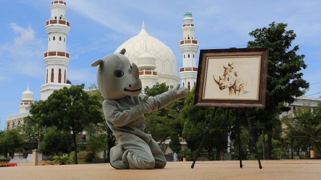 Pemuda dengan kostum badak sumatera menunjukkan lukisan badak sumatera saat kegiatan kampanye kreatif memperingati hari badak sedunia di Taman Ratu Safiatuddin, Banda Aceh, Aceh, Rabu (22/9/2021). ANTARA FOTO/Syifa Yulinnas