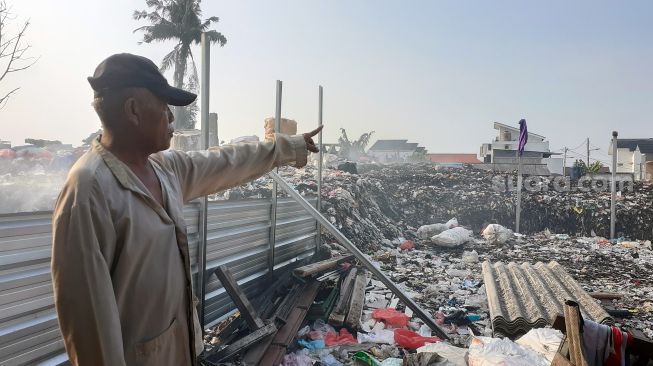 Darkim, pengelola lapak sampah di TPS Jalan Wijaya Kusuma Ujung X Gang Sawo 1 RT 13 RW 1 Kelurahan Pondok Betung, Pondok Aren, Kota Tangerang Selatan, menunjuk tumpukan sampah setinggi 3 meter, Selasa (21/9/2021). [SuaraJakarta.id/Wivy Hikmatullah]