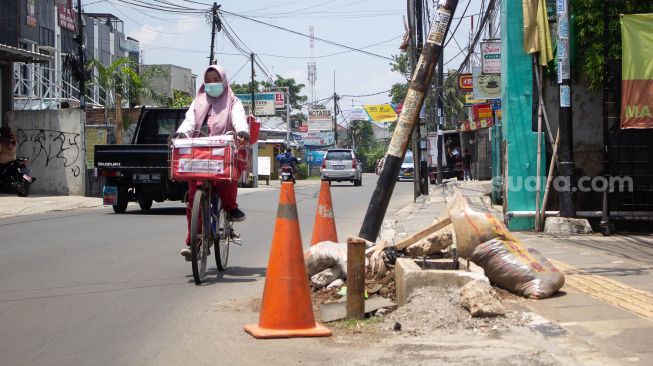 Pesepeda melintas di samping tiang miring di Jl Wr Supratman Ciputat Timur, Tangerang Selatan. Rabu (22/9).  [Suara.com/ Hilal Rauda Fiqry]