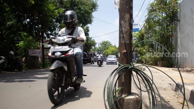 Pengendara sepeda motor melintas di samping tiang miring di Jl Wr Supratman Ciputat Timur, Tangerang Selatan. Rabu (22/9).  [Suara.com/ Hilal Rauda Fiqry]