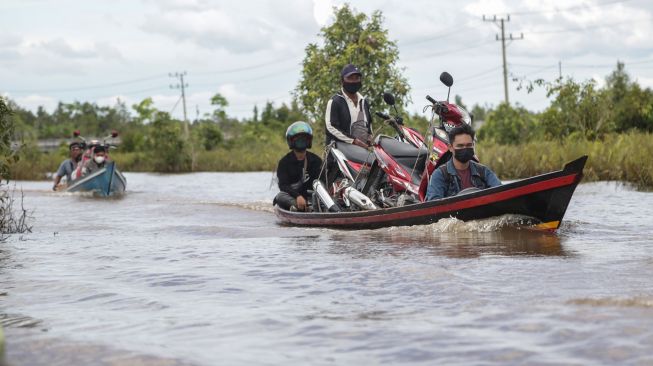 Pengendara motor menggunakan perahu bermesin (klotok) untuk melintasi banjir yang merendam di jalan trans Kalimantan Bukit Rawi, Pulang Pisau, Kalimantan Tengah, Kamis (23/9/2021). ANTARA FOTO/Makna Zaezar
