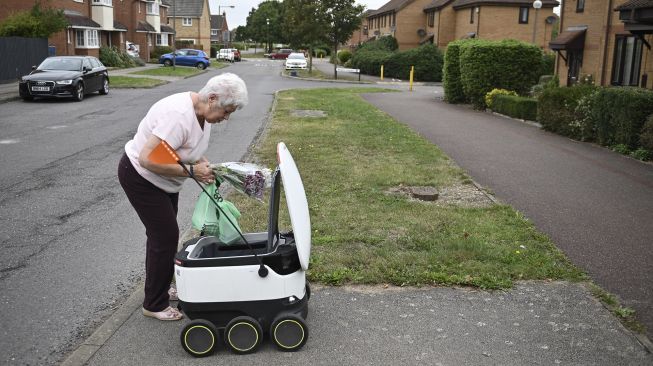 Sheila (71) mengambil kiriman dari robot otonom bernama Starship yang mengantarkan bahan makanan dari supermarket Co-op terdekat di Milton Keynes, Inggris, pada (20/9/2021). [DANIEL LEAL-OLIVAS / AFP]