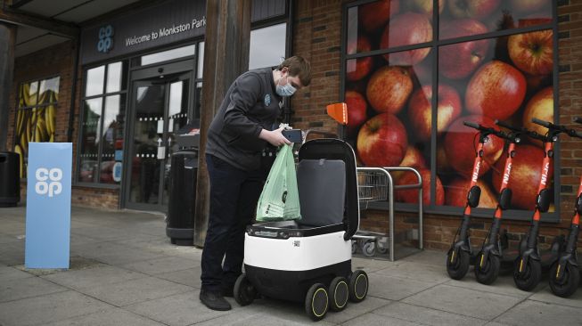 Seorang pekerja toko memuat tas di dalam robot otonom yang disebut Starship sebelum mengirimkan bahan makanan di Milton Keynes, Inggris, pada (20/9/2021). [DANIEL LEAL-OLIVAS / AFP]