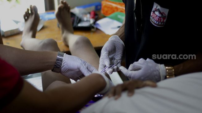 Petugas medis menangani seorang anak yang mengikuti sunatan massal yang digelar di Binong Permai, Kabupaten Tangerang, Banten, Sabtu (25/9/2021). [Suara.com/ Hilal Rauda Fiqry]