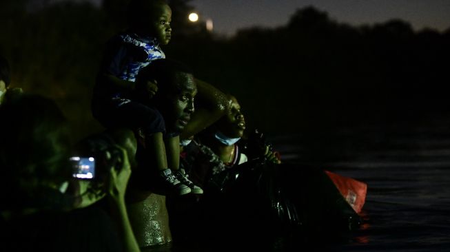 Migran Haiti menyeberangi Sungai Rio Grande di perbatasan Meksiko-AS, pada (23/9/2021). [PEDRO PARDO / AFP]