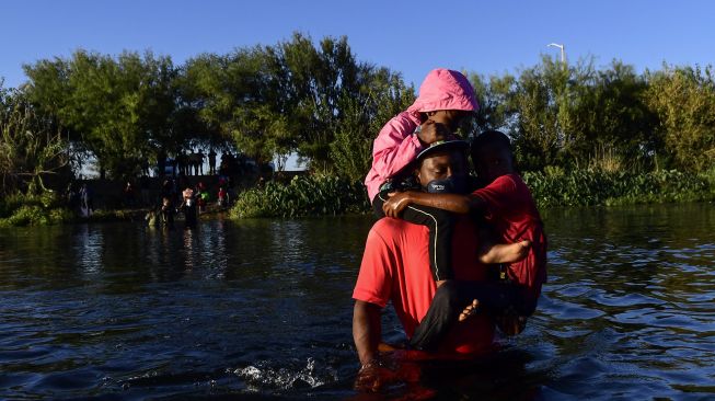 Migran Haiti menyeberangi Sungai Rio Grande di perbatasan Meksiko-AS, pada (23/9/2021). [PEDRO PARDO / AFP]