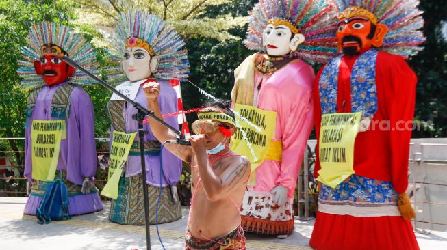 Seorang aktivis menunjukkan aksi teaterikal sambil memegang poster saat melakukan aksi protes terkait perubahan iklim di Kawasan Dukuh Atas, Jakarta Pusat, Minggu (26/9/2021). [Suara.com/Alfian Winanto]