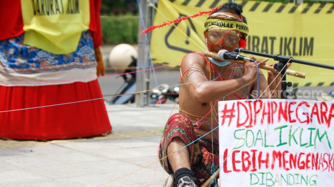 Seorang aktivis menunjukkan aksi teaterikal sambil memegang poster saat melakukan aksi protes terkait perubahan iklim di Kawasan Dukuh Atas, Jakarta Pusat, Minggu (26/9/2021). [Suara.com/Alfian Winanto]