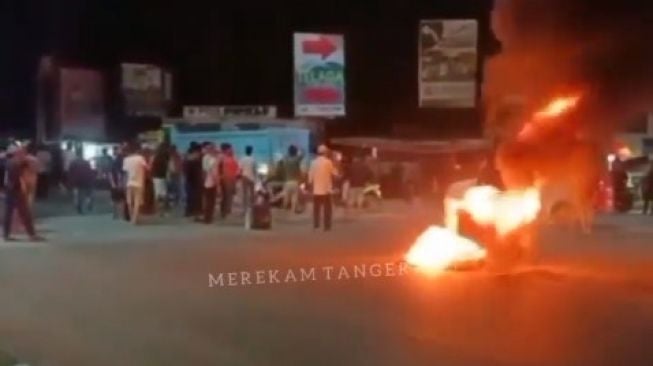 Massa aksi demo melakukan bakar ban dan menutup akses Jalan Raya Parung Panjang, tepatnya di pertigaan Dasim, Cirarab, Kecamatan Legok, Kabupaten Tangerang, Sabtu (25/9/2021) malam. [Tangkapan layar Instagram@merekamtangerang]