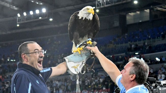 Pelatih Lazio, Maurizio Sarri (kiri) merayakan kemenangan dengan maskot elang Lazio Olympia pada akhir pertandingan lanjutan Liga Italia antara Lazio vs Roma di stadion Olimpico di Roma pada 26 September 2021.Vincenzo PINTO / AFP.