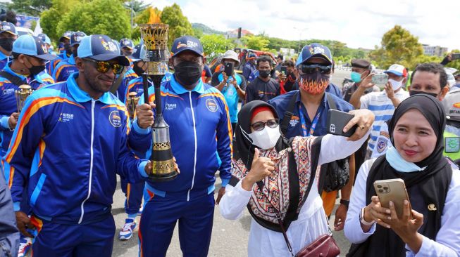 
Warga berfoto dengan mantan atlet sepak bola Ortisan Solosa (kiri) dan Roni Wabia yang membawa Api PON XX di Bandara DEO Kota Sorong, Papua Barat, Senin (27/09/2021). ANTARA FOTO/Olha Mulalinda