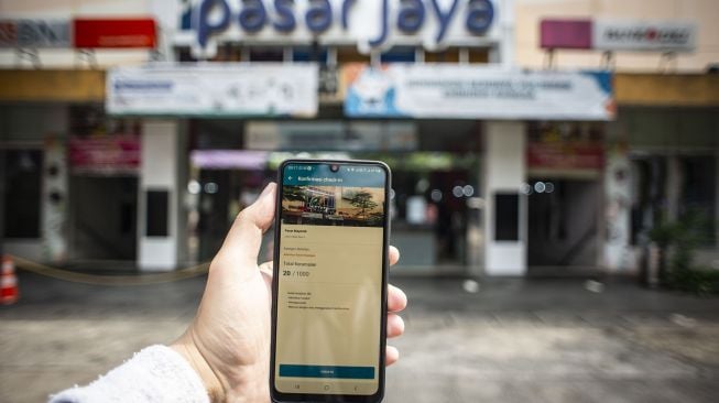 Pengunjung menunjukkan layar gawai usai memindai kode batang (QR Code) menggunakan aplikasi PeduliLindungi di pintu masuk Pasar Mayestik, Kebayoran Baru, Jakarta, Jumat (1/10/2021).  ANTARA FOTO/Aprillio Akbar