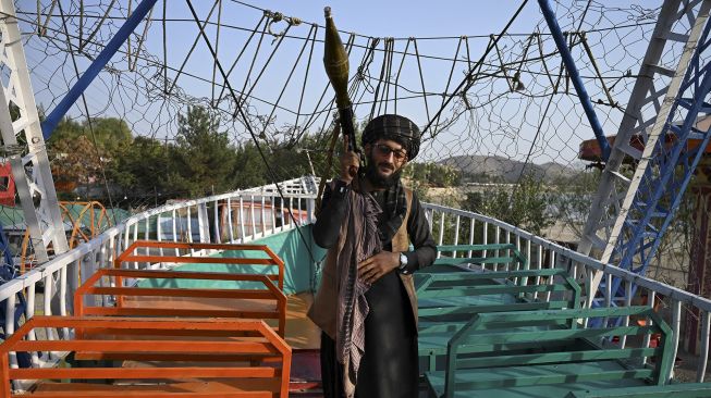 Seorang pejuang Taliban yang membawa peluncur roket (RPG) berdiri di atas kapal bajak laut di sebuah taman bermain di Danau Qargha, Kabul, Afghanistan, pada (28/9/2021). [WAKIL KOHSAR / AFP]