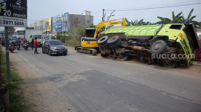 Sejumlah kendaraan melintas di samping truk yang terperosok galian pipa PDAM di jalan raya Legok, Kabupaten Tangerang, Banten, Kamis (7/10).  [Suara.com/ Hilal Rauda Fiqry] 