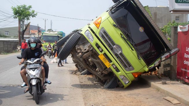 Sejumlah pengendara roda dua melintas di samping truk yang terperosok galian pipa PDAM di jalan raya Legok, Kabupaten Tangerang, Banten, Kamis (7/10).  [Suara.com/ Hilal Rauda Fiqry] 