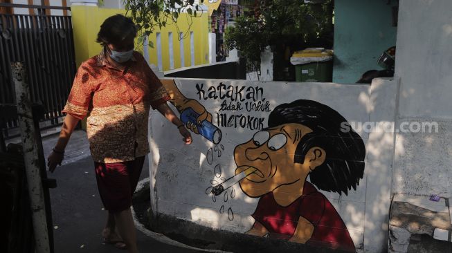 Warga berjalan melintasi mural larangan merokok di RW.06 Kelurahan Kayu Manis, Matraman, Jakarta, Jumat (8/10/2021). [Suara.com/Angga Budhiyanto]