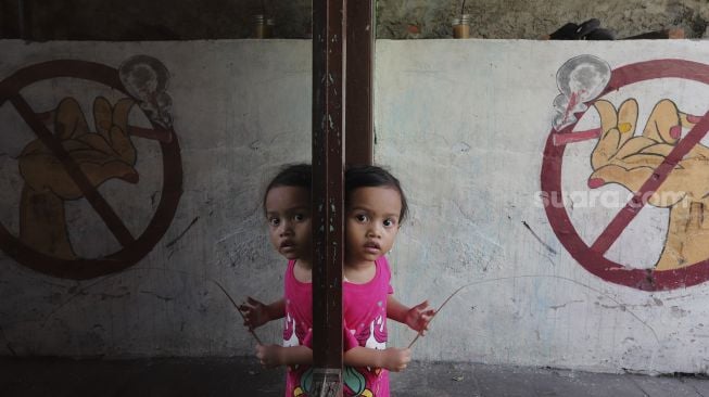 Seorang anak berdiri di dekat mural larangan merokok di RW.06 Kelurahan Kayu Manis, Matraman, Jakarta, Jumat (8/10/2021). [Suara.com/Angga Budhiyanto]