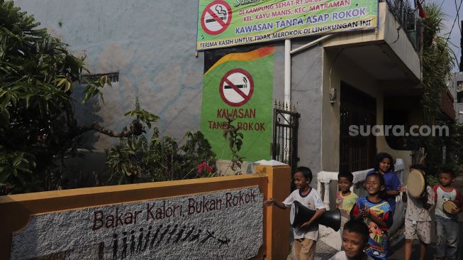 Sejumlah anak berjalan melintasi mural larangan merokok di RW.06 Kelurahan Kayu Manis, Matraman, Jakarta, Jumat (8/10/2021). [Suara.com/Angga Budhiyanto]