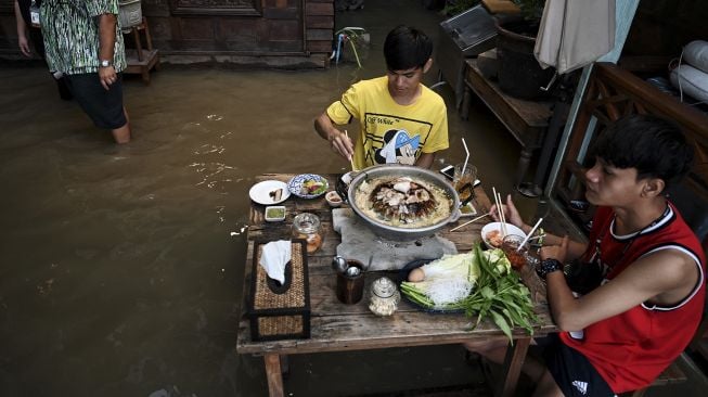 Pengunjung menikmati makan malam di Kafe Antik Chaopraya, saat air banjir dari Sungai Chao Phraya mengalir ke restoran di provinsi Nonthaburi, Bangkok, Thailand, pada (7/10/2021). [Lillian SUWANRUMPHA / AFP]