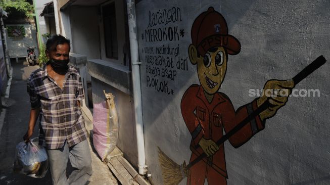 Warga berjalan melintasi mural larangan merokok di RW.06 Kelurahan Kayu Manis, Matraman, Jakarta, Jumat (8/10/2021). [Suara.com/Angga Budhiyanto]