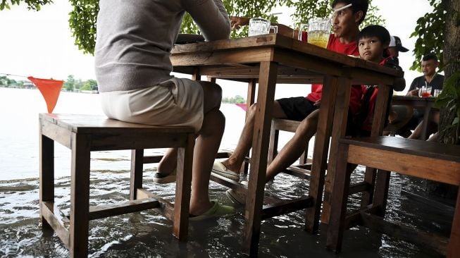 Pengunjung menikmati makan malam di Kafe Antik Chaopraya, saat air banjir dari Sungai Chao Phraya mengalir ke restoran di provinsi Nonthaburi, Bangkok, Thailand, pada (7/10/2021). [Lillian SUWANRUMPHA / AFP]