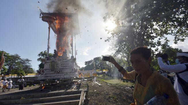 Warga negara asing (WNA) menyaksikan prosesi pembakaran peti berbentuk lembu atau sapi putih yang berisi jenazah Ida Pedanda Nabe Gede Dwija Ngenjung saat upacara Ngaben di kawasan Sanur, Denpasar, Bali, Jumat (8/10/2021). [ANTARA FOTO/Nyoman Hendra Wibowo]