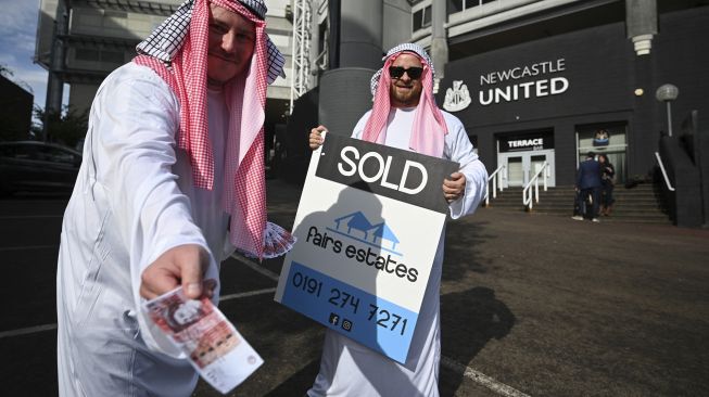 Pendukung Newcastle United mengenakan jubah berpose dengan plakat 'dijual' saat mereka merayakan penjualan klub ke konsorsium yang dipimpin Saudi, di luar stadion klub di St James' Park, Newcastle upon Tyne, Inggris, pada (8/10/2021). [OLI SCARFF / AFP]