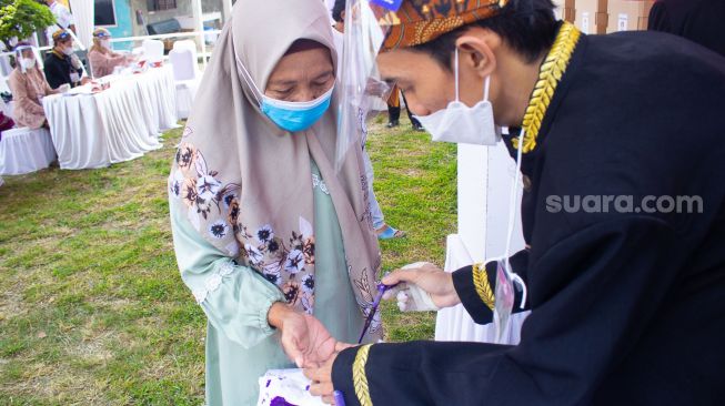 Petugas TPS memberikan tinta ke jari warga setelah melakukan pencoblosan di TPS 04 Desa Bojong Kamal, Kabupaten Tangerang, Banten, Minggu 10/10. ( Suara.com/ Hilal Rauda Fiqry) 
