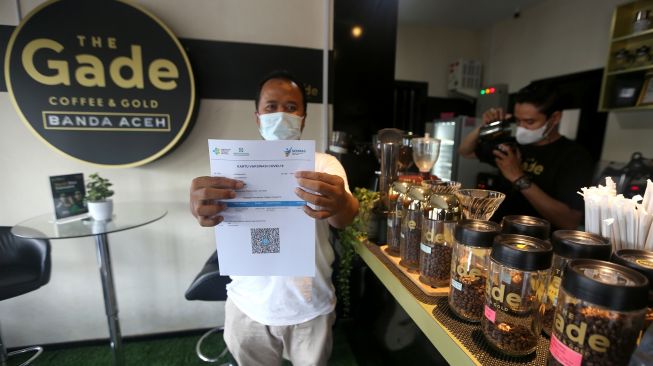 Pengunjung salah satu warung kopi (warkop) memperlihatkan sertifikat vaksin COVID-19 seusai mendapatkan suntikan yang digelar Polda Aceh di Banda Aceh, Aceh, Minggu (10/10/2021).ANTARA FOTO / Irwansyah Putra