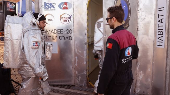 Seorang astronot dari tim Eropa dan Israel berjalan dengan mengenakan pakaian antariksa bersiap untuk memasuki habitat tertutup selama misi pelatihan untuk planet Mars di sebuah situs yang mensimulasikan stasiun di luar lokasi di Kawah Ramon, Mitzpe Ramon, Gurun Negev, Israel, pada (10/10/2021). [JACK GUEZ / AFP]