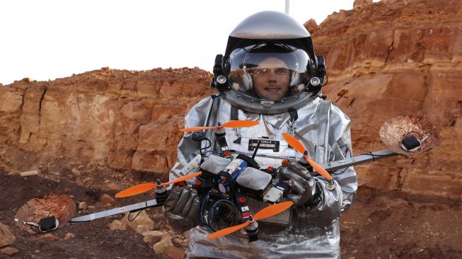 Seorang astronot dari tim Eropa dan Israel mengenakan pakaian antariksa memegang 'drone quadcopter' selama misi pelatihan untuk planet Mars di sebuah situs yang mensimulasikan stasiun di luar lokasi di Kawah Ramon, Mitzpe Ramon, Gurun Negev, Israel, pada (10/10/2021). [JACK GUEZ / AFP]