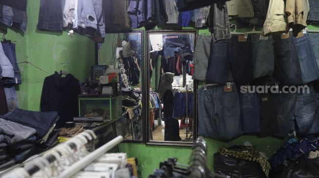 Refleksi pedagang merapikan pakaian bekas layak pakai (thrifting) di Pasar Kebayoran Lama, Jakarta, Rabu (13/10/2021). [Suara.com/Angga Budhiyanto]