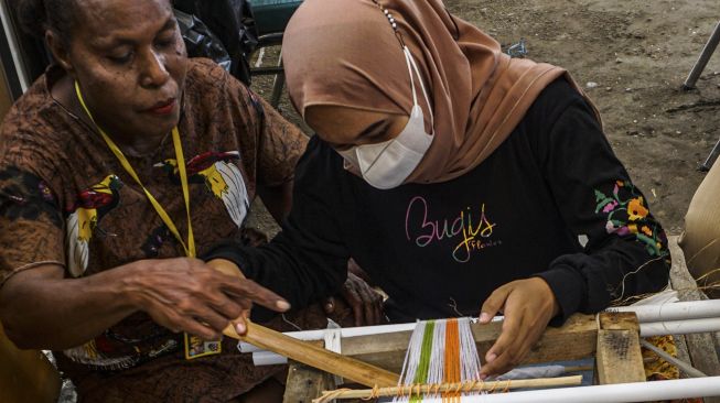 Penenun kain tervo Salonika Ambani (kiri) mengajarkan cara menenun kepada seorang wisatawan di sebuah stan Pameran dan Pagelaran Budaya Nasional di Holtekamp Jayapura, Papua, Kamis (14/10/2021). [ANTARA FOTO/Indrayadi TH]