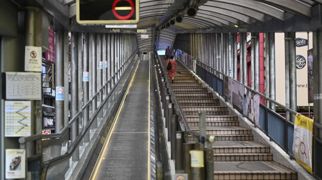 Seorang pejalan kaki berjalan di samping eskalator Mid-Levels yang ditutup di kawasan pusat bisnis di Hong Kong, pada (13/10/2021). [PETER PARKS / AFP]